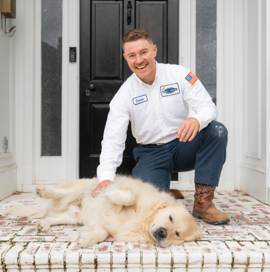 Person kneeling on a porch, wearing a work uniform with a name tag and U.S. flag patch, petting a golden retriever lying on the brick steps. Black front door in the background.