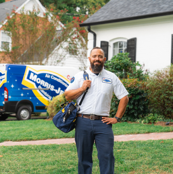 A uniformed technician stands outside a house with a Morris-Jenkins van in the background, holding a tool bag and smiling.