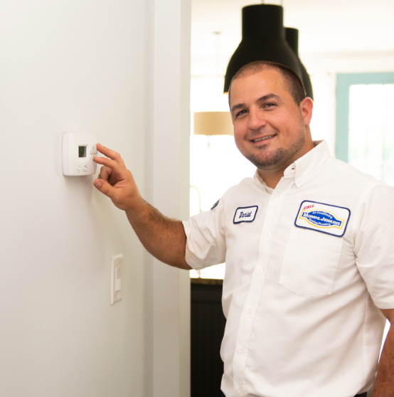 A person in a white uniform shirt adjusts a thermostat on a white wall in a home environment.