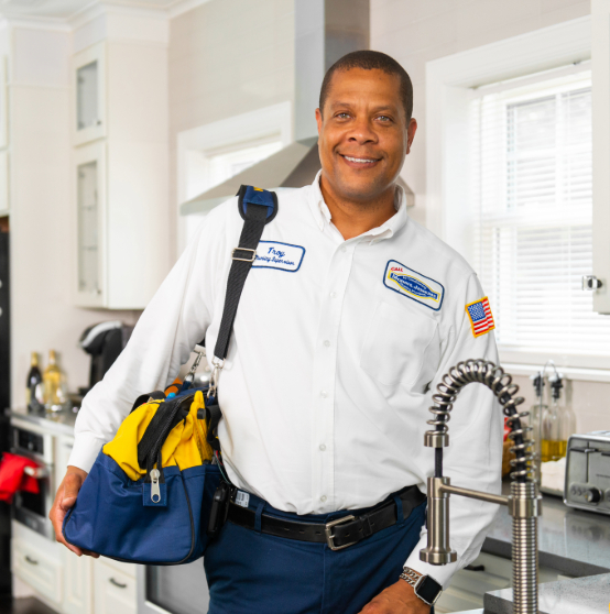 A man in a uniform stands in a kitchen holding a tool bag.