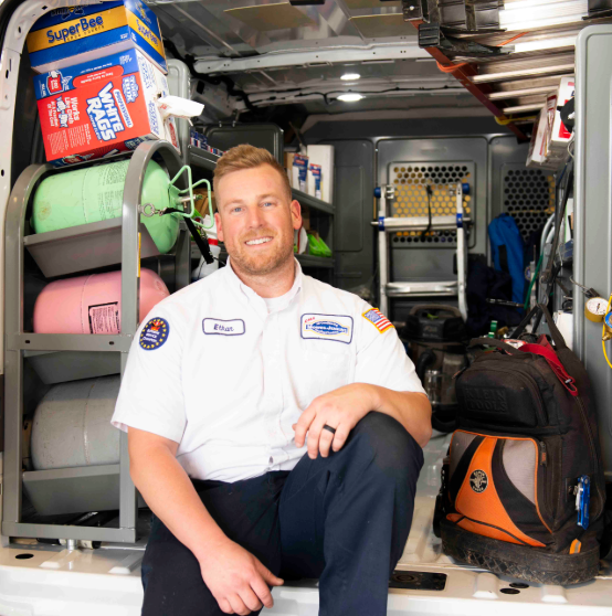 Person in a uniform sitting in a work van, with tanks, tools, and equipment in the background.