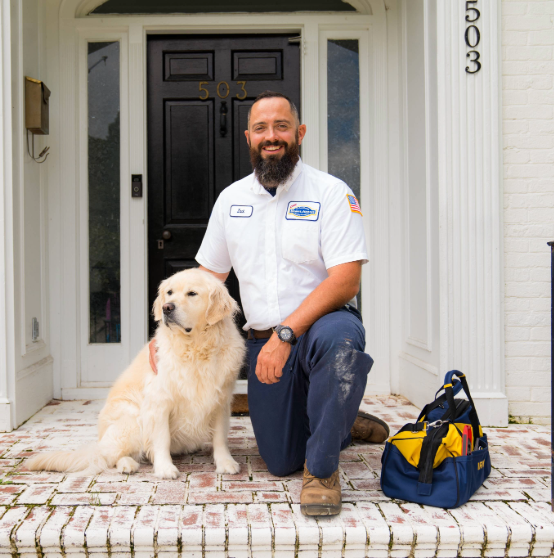 Bearded man in a white uniform kneels beside a golden retriever on a porch. A tool bag rests next to him. House number 503 visible on the door.